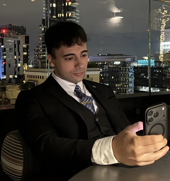 Andrei al tavolo di un ristorante in alto, con lo skyline della città dietro.