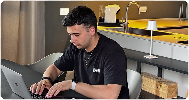 Andrei al portatile, seduto al tavolo di una cucina gialla.